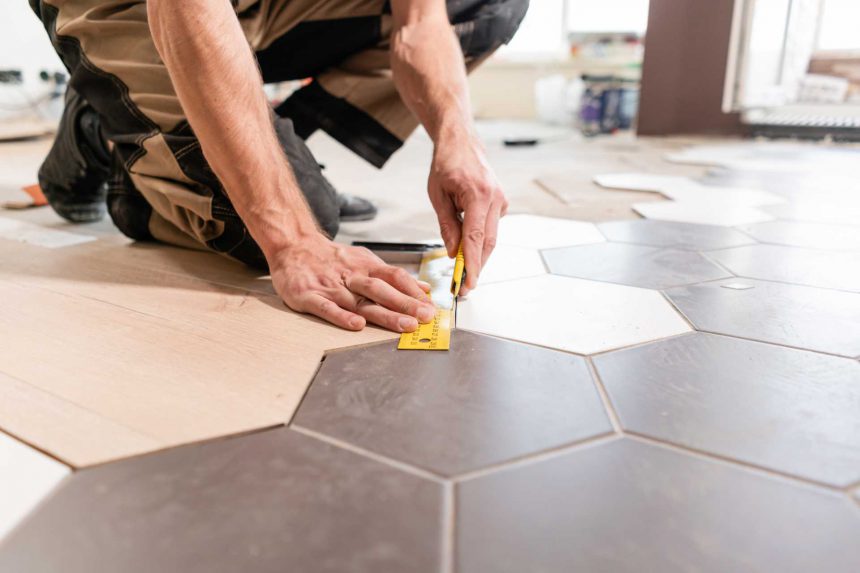 Male worker makes measurements and installing new wooden laminate flooring. The combination of wood panels of laminate and ceramic tiles in the form of honeycomb. Kitchen renovation. Professional Tile Installation Benefits – Robert Tile Installation, Chicago IL